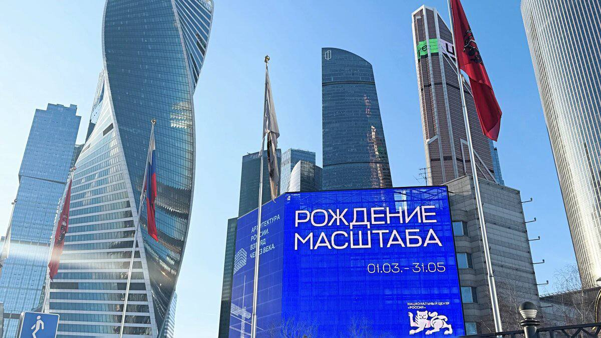 Наружная афиша выставки «Рождение масштаба» на фоне высотной архитектуры